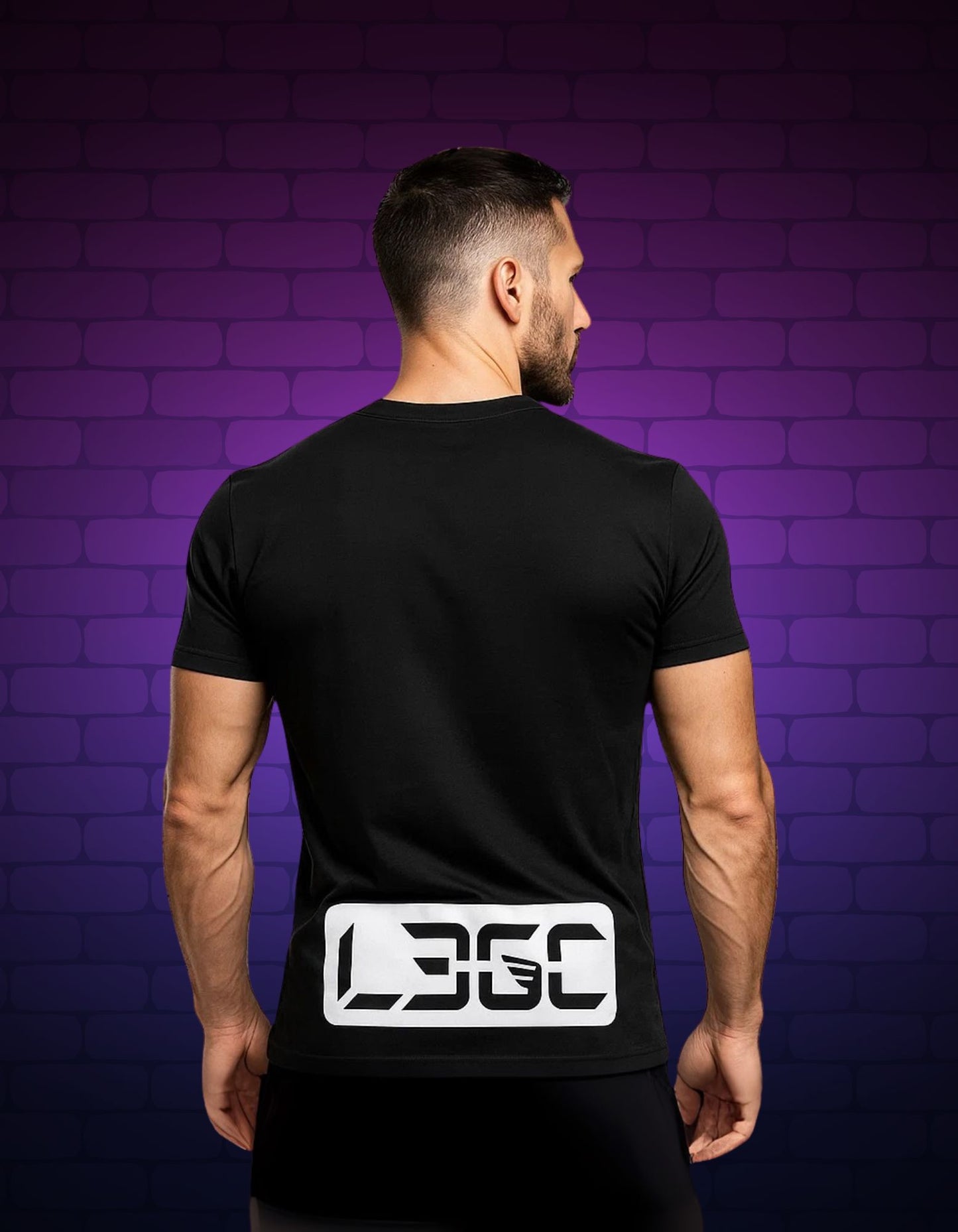Man wearing a black t-shirt with a logo on the back against a purple brick wall.