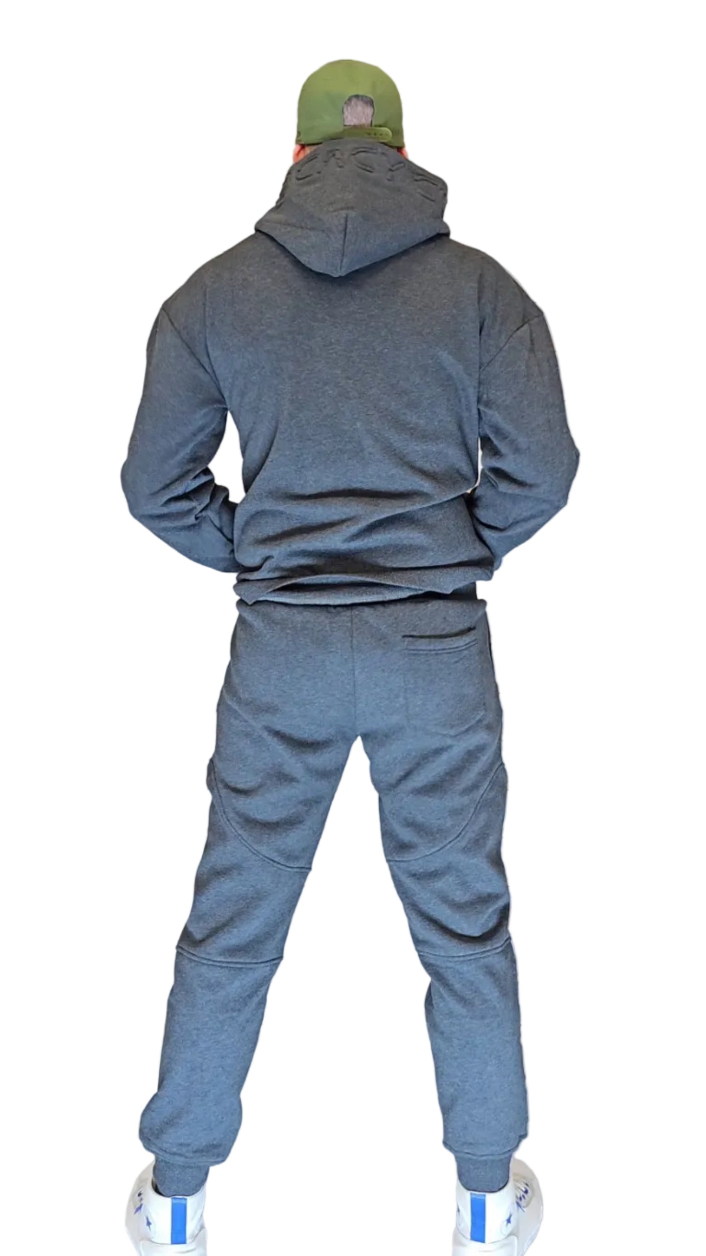 Person wearing a gray tracksuit and green cap standing in front of a metallic shutter.