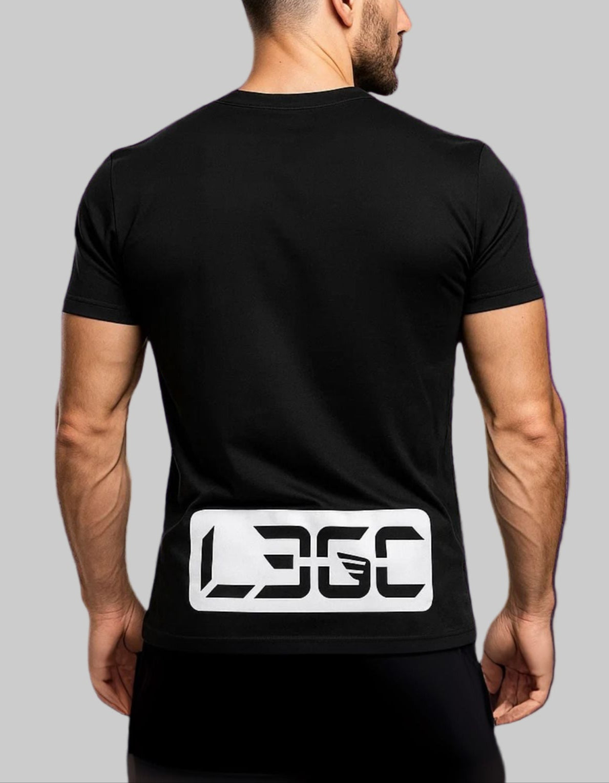 Man wearing a black t-shirt with a logo on the back against a purple brick wall.