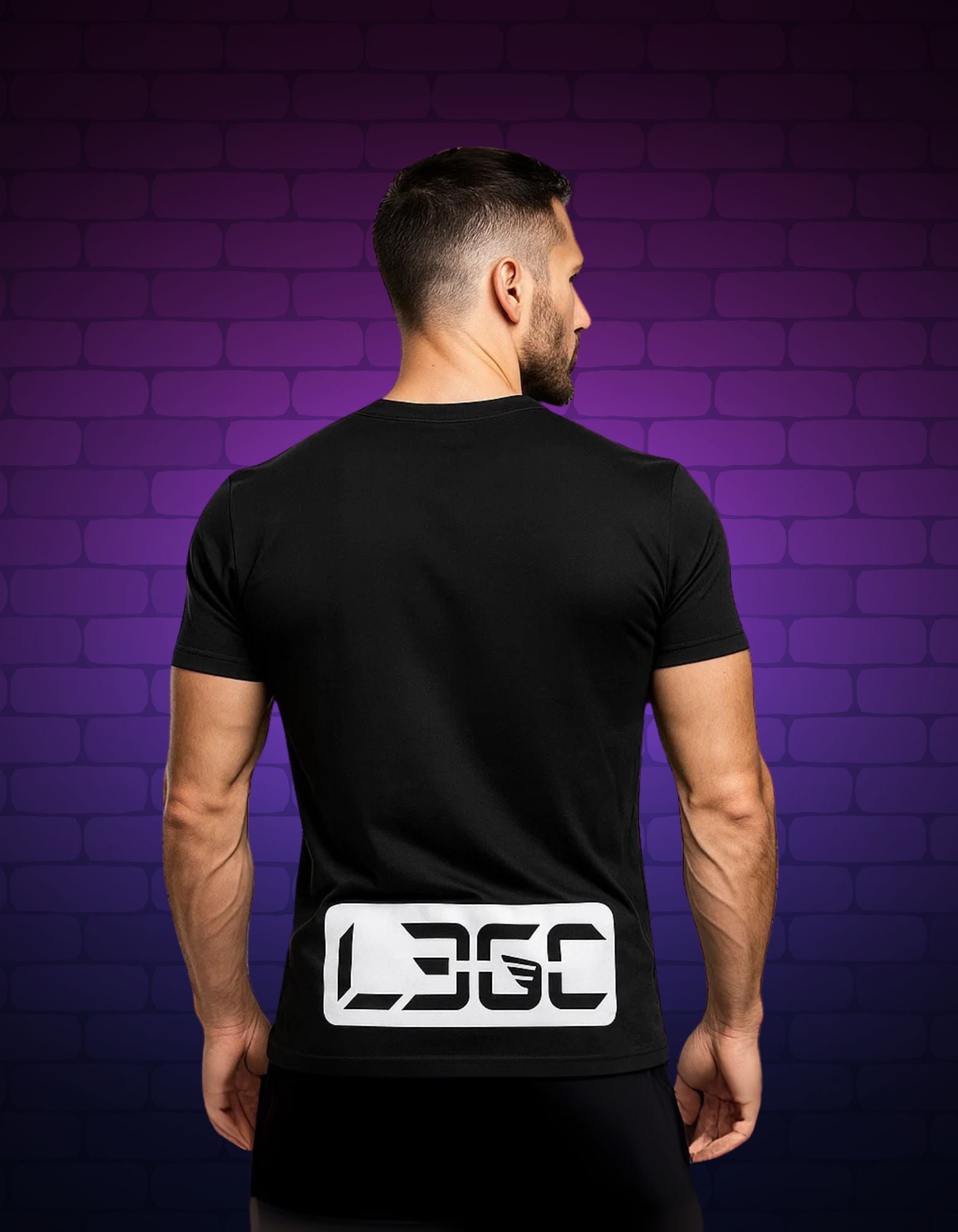 Man wearing a black t-shirt with a logo on the back against a purple brick wall.