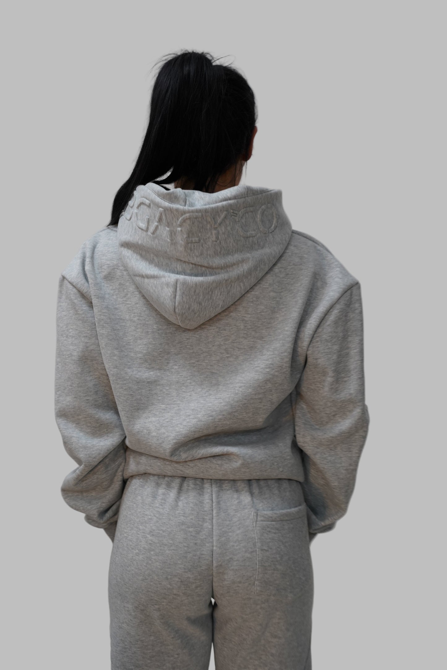 Person wearing a gray hoodie and pants on a white floor.