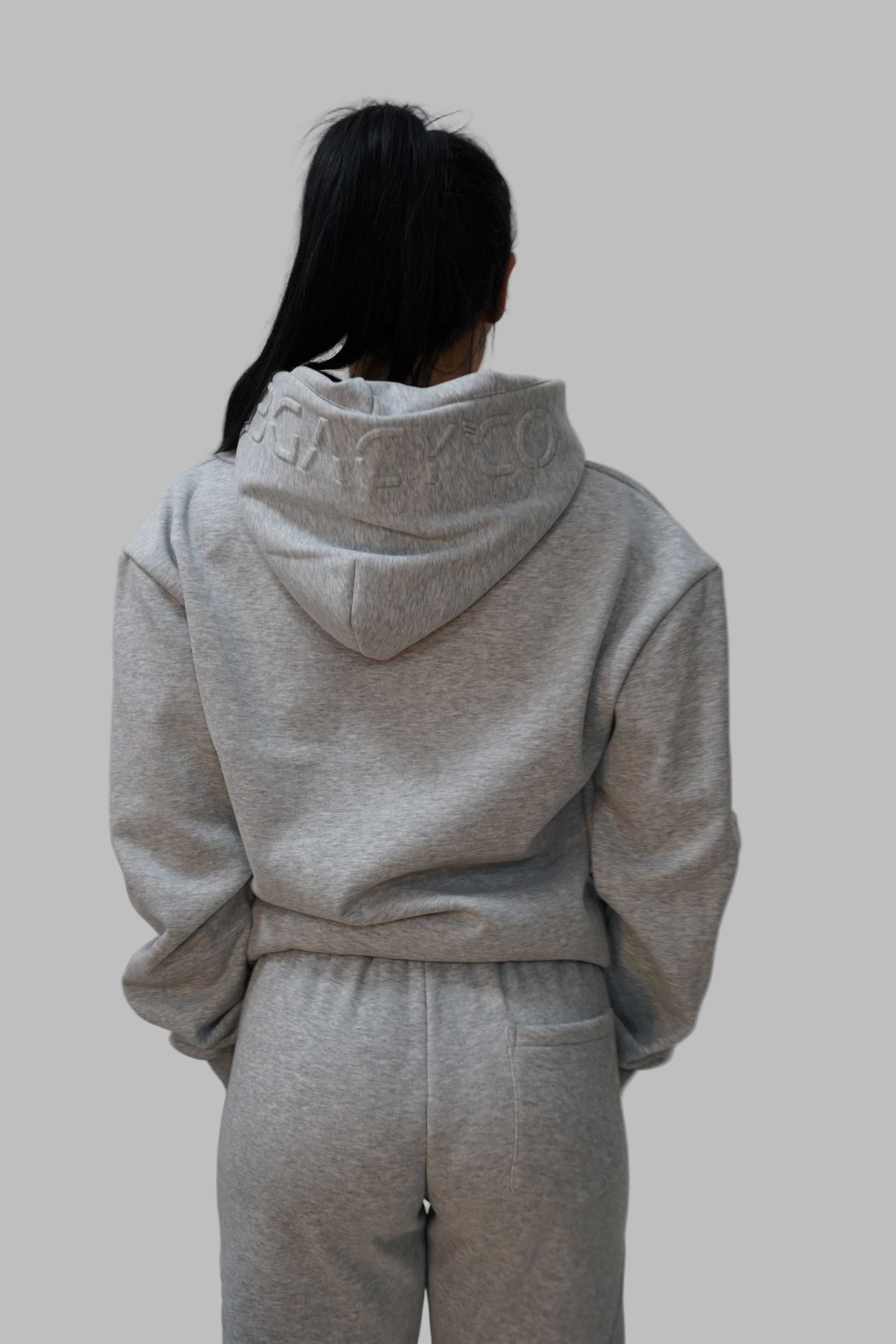 Person wearing a gray hoodie and pants on a white floor.