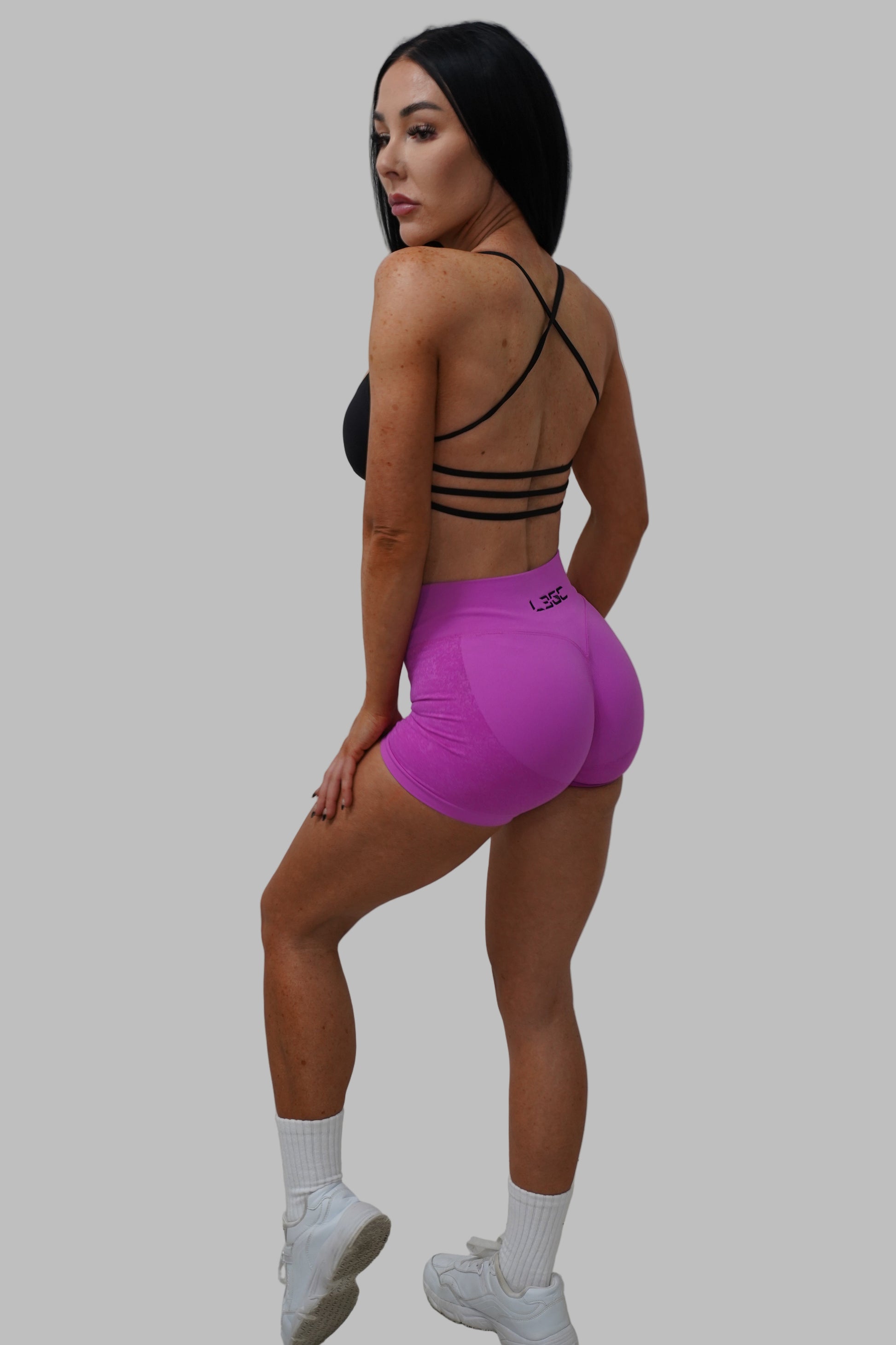 Person wearing a black bikini top and purple shorts on a white floor.