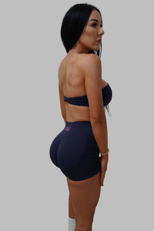 Woman in a navy blue sports bra and leggings against a plain background