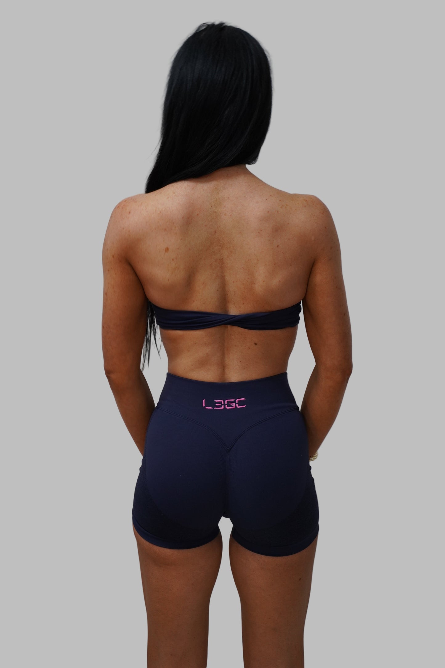 woman wearing dark athletic shorts with a visible brand logo on a plain background